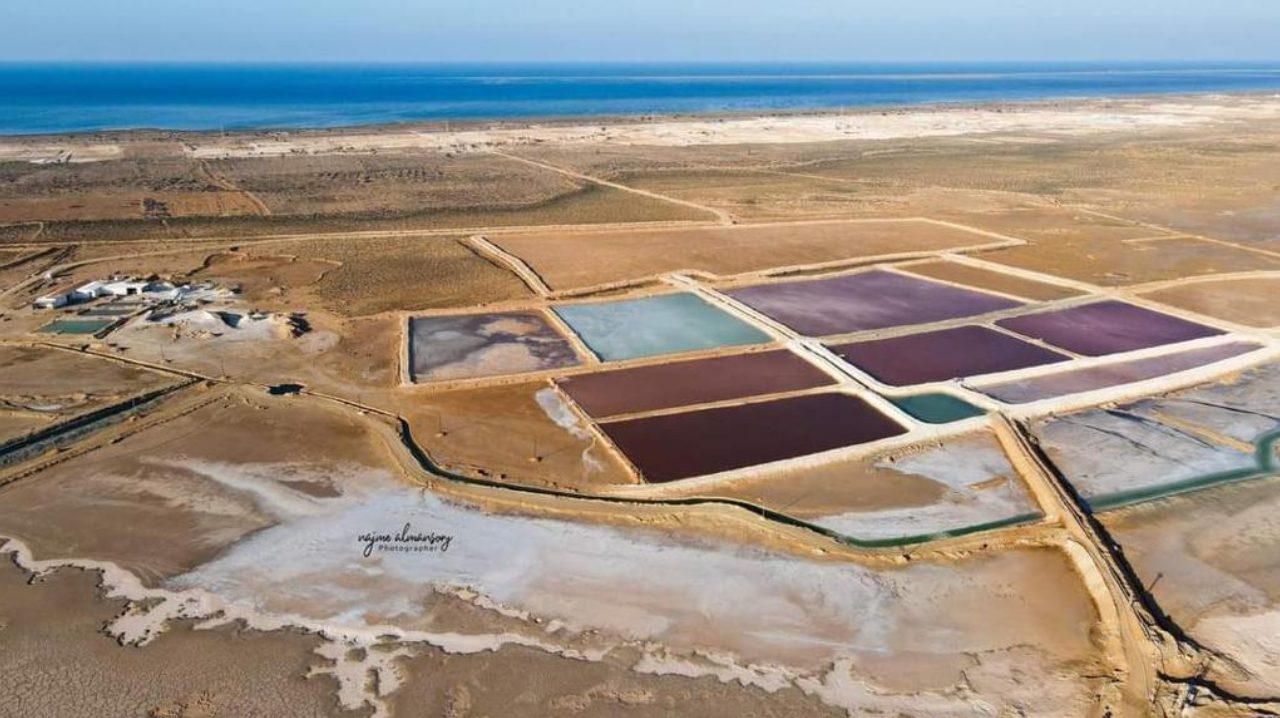 Aerial view of the Al Mozan solar salt works at Ras Ajdir, Libya: evaporation basins in brine red and jade with the Mediterranean Sea behind